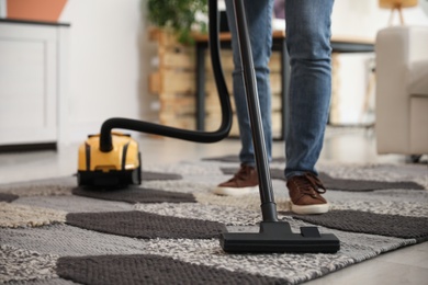 Photo of Young man cleaning carpet with vacuum cleaner at home, closeup