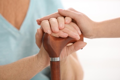Photo of Nurse comforting elderly woman with cane against light background, closeup. Assisting senior generation