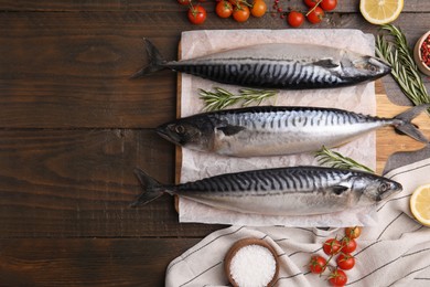 Photo of Raw mackerel, tomatoes and rosemary on wooden table, flat lay. Space for text