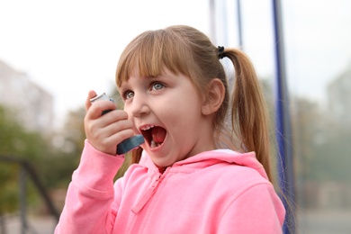 Little girl using asthma inhaler outdoors. Health care