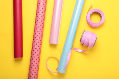 Photo of Rolls of colorful wrapping papers and ribbons on yellow background, flat lay