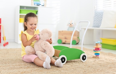 Photo of Cute little girl playing with teddy bear on floor at home. Soft toy