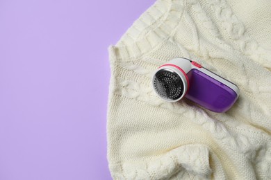 Photo of Modern fabric shaver and woolen sweater on purple background, top view. Space for text