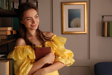 Photo of Beautiful young woman in yellow dress with book near home library indoors