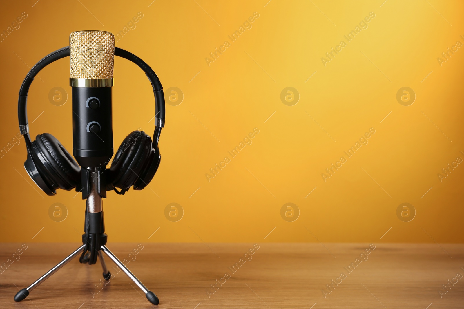 Photo of Microphone and modern headphones on wooden table against orange background, space for text