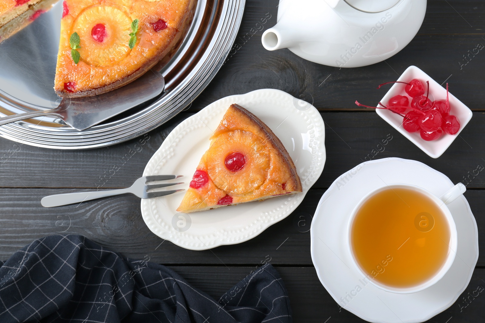 Photo of Delicious cut pineapple pie with cherry and tea served on black wooden table, flat lay