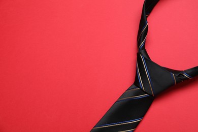 Striped necktie on red background, top view. Space for text