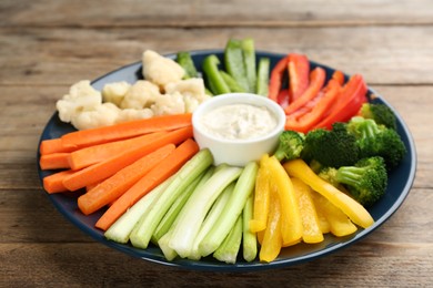 Plate with celery sticks, other vegetables and dip sauce on wooden table, closeup