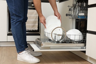 Man loading dishwasher with plates indoors, closeup