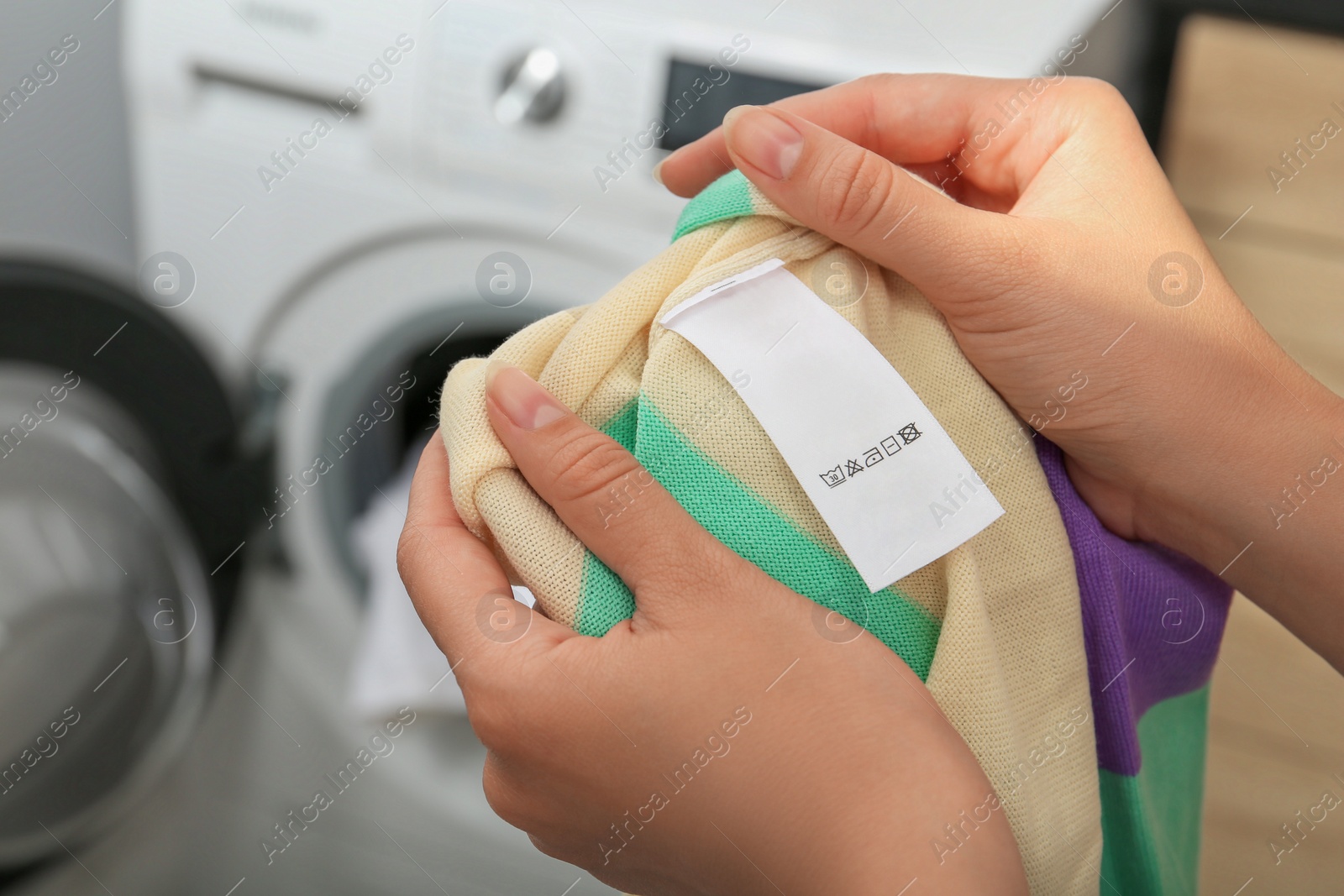 Photo of Woman holding apparel with blank clothing label at home, closeup