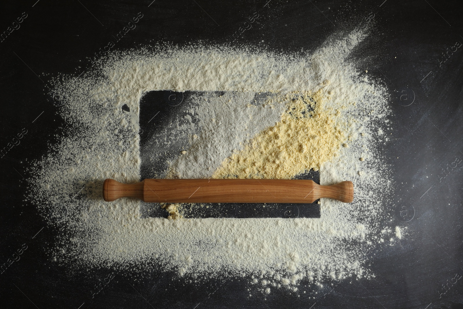 Photo of Flour and rolling pin on black table, top view