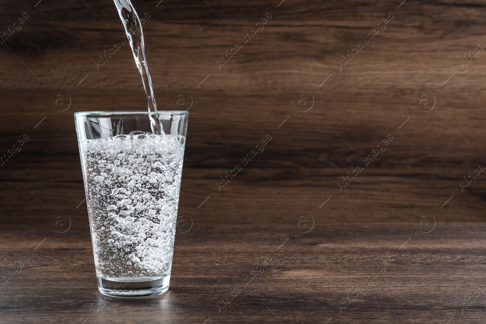 Photo of Pouring soda water into glass on wooden table. Space for text