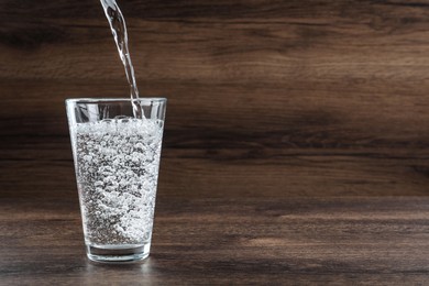 Photo of Pouring soda water into glass on wooden table. Space for text