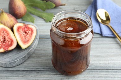 Jar of tasty sweet jam and fresh figs on grey table