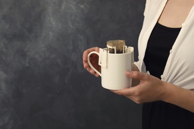 Photo of Woman holding cup with drip coffee bag on grey background, closeup. Space for text
