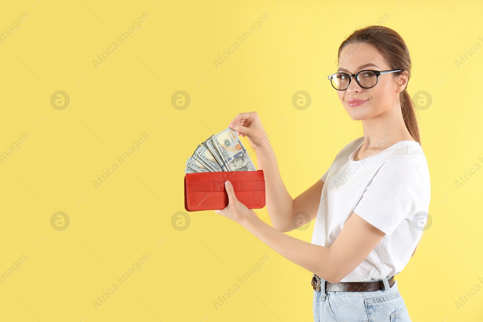 Photo of Young woman with wallet full of money on yellow background