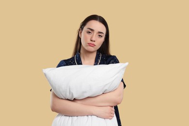 Tired young woman with pillow on beige background. Insomnia problem