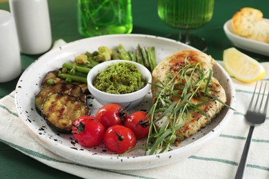 Photo of Tasty chicken, vegetables with tarragon and pesto sauce served on table, closeup