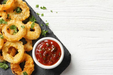 Photo of Homemade crunchy fried onion rings with tomato sauce on wooden table, top view. Space for text