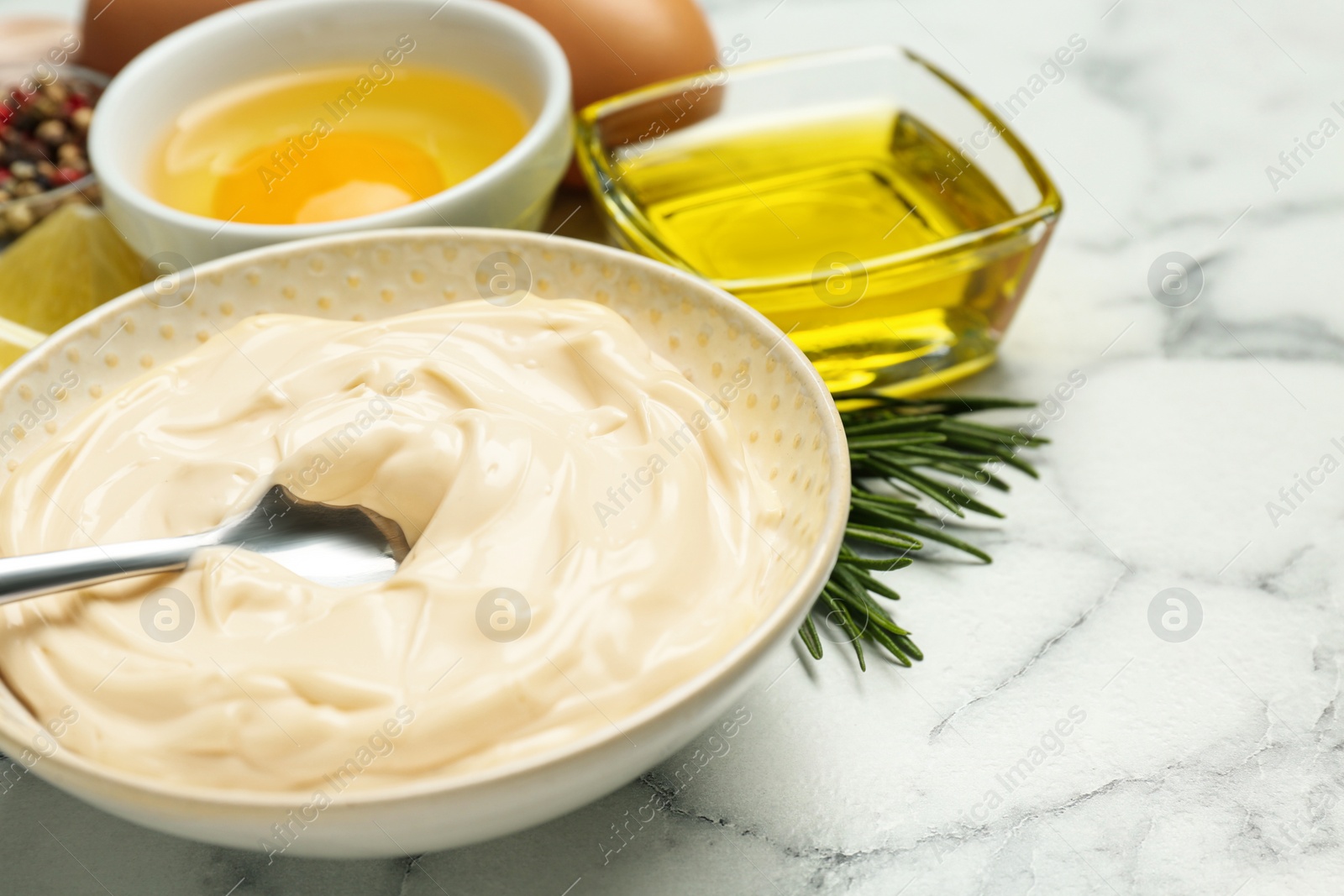 Photo of Bowl with fresh mayonnaise and ingredients on white marble table, closeup. Space for text