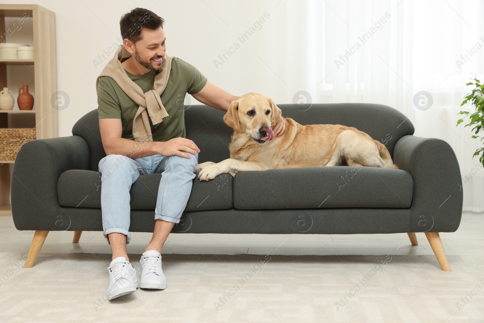 Photo of Happy man sitting on sofa with his cute Labrador Retriever at home