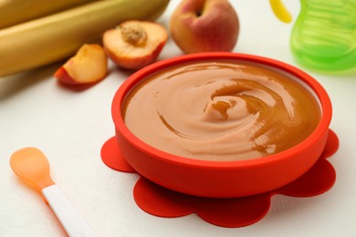 Photo of Bowl of tasty pureed baby food and ingredients on white table