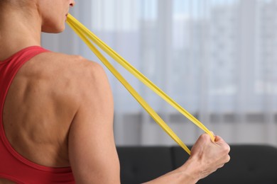 Photo of Woman doing exercise with fitness elastic band indoors, closeup