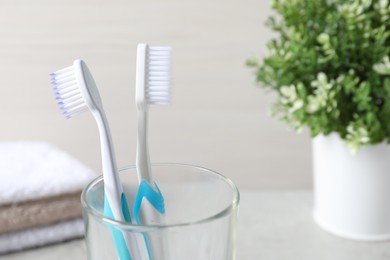 Photo of Plastic toothbrushes in glass holder against light background, closeup
