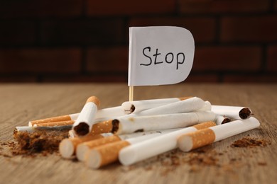 Photo of Pile of cigarettes and flag with word Stop on wooden table, closeup. No smoking concept