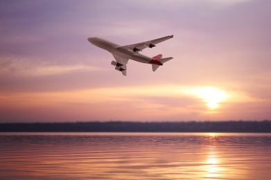 Modern airplane flying over river during sunset