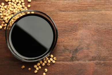 Photo of Soy sauce in bowl and soybeans on wooden table, flat lay. Space for text