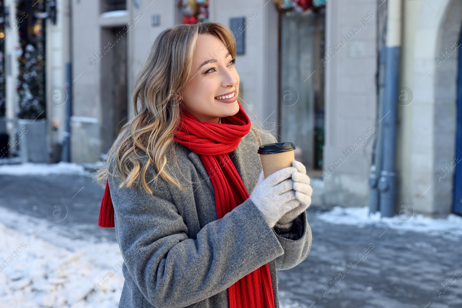 Photo of Portrait of smiling woman with paper cup of coffee on city street in winter