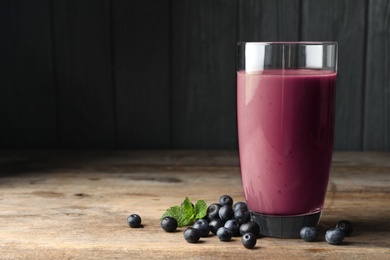 Photo of Tasty acai drink in glass and berries on wooden table. Space for text