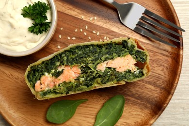 Piece of delicious strudel with salmon and spinach served on light wooden table, top view