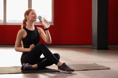 Photo of Athletic young woman with bottle of water on mat in gym, space for text