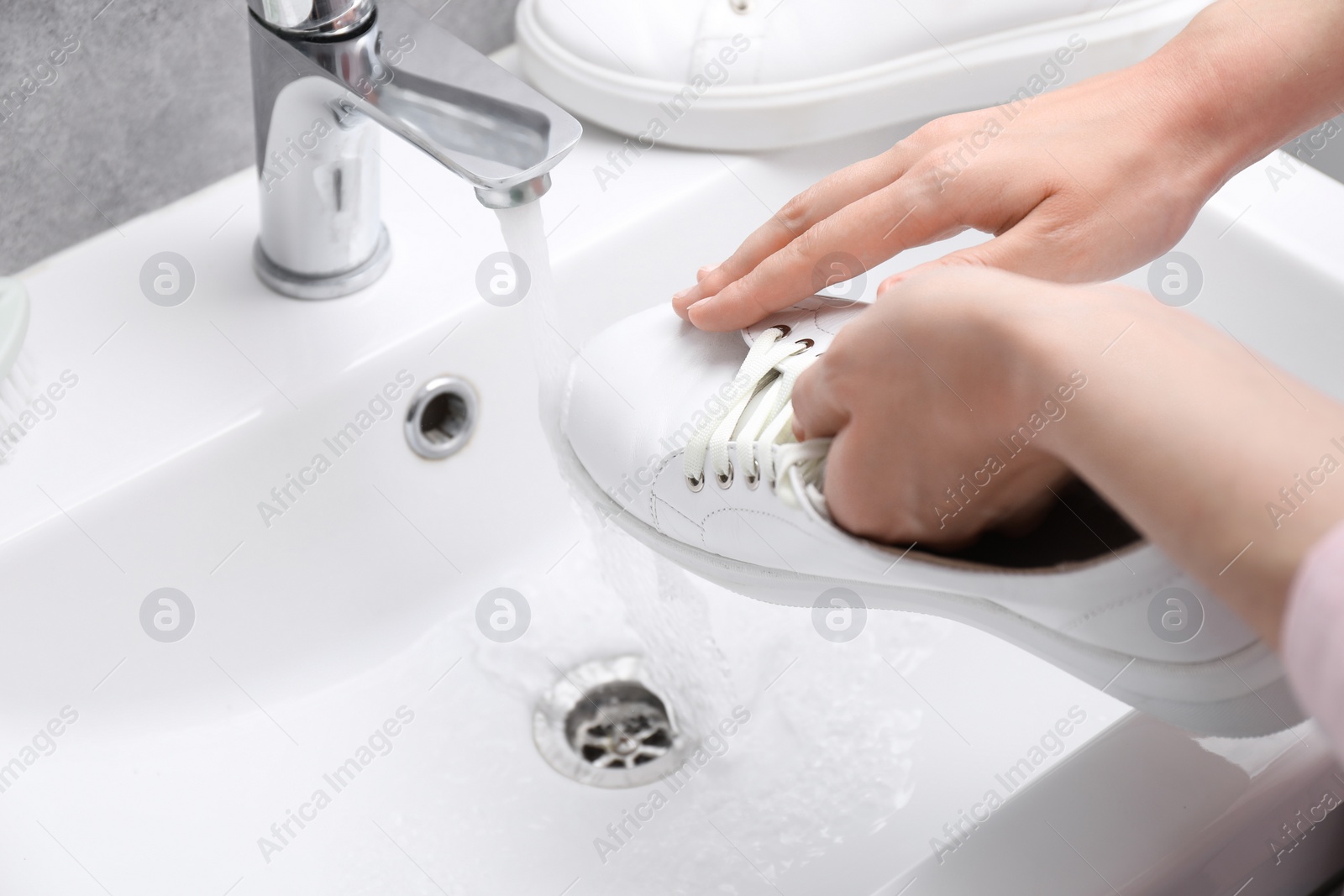 Photo of Woman washing stylish sneakers in sink, closeup