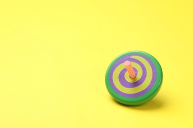 Photo of One colorful spinning top on yellow background, space for text