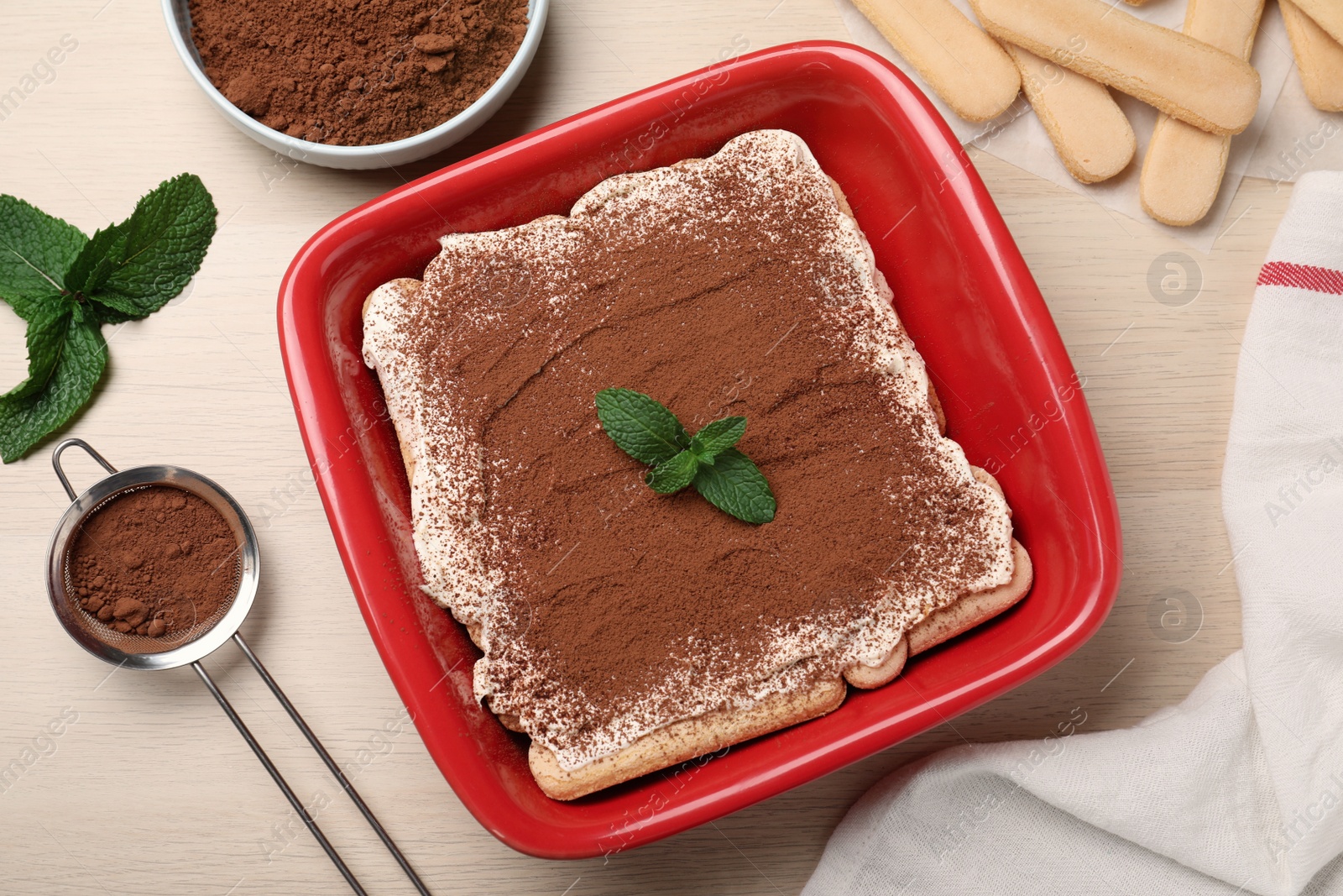 Photo of Red bowl with delicious tiramisu cake on white wooden table, flat lay