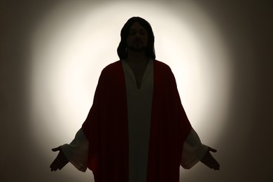Silhouette of Jesus Christ with outstretched arms on color background