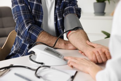 Photo of Doctor measuring blood pressure of man at table indoors, closeup