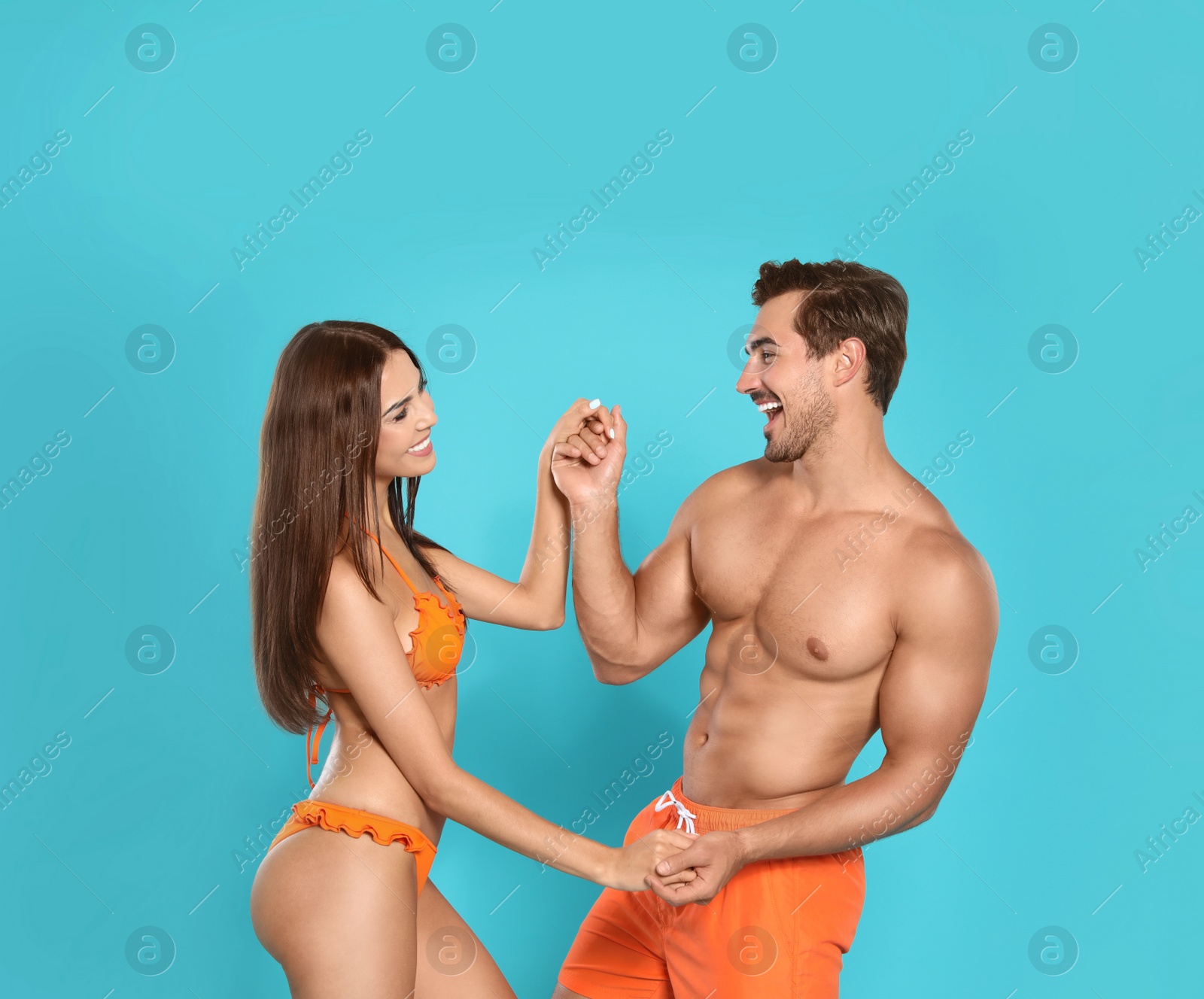 Photo of Young attractive couple in beachwear dancing on blue background