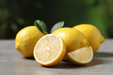 Fresh lemons and green leaves on grey table outdoors, closeup