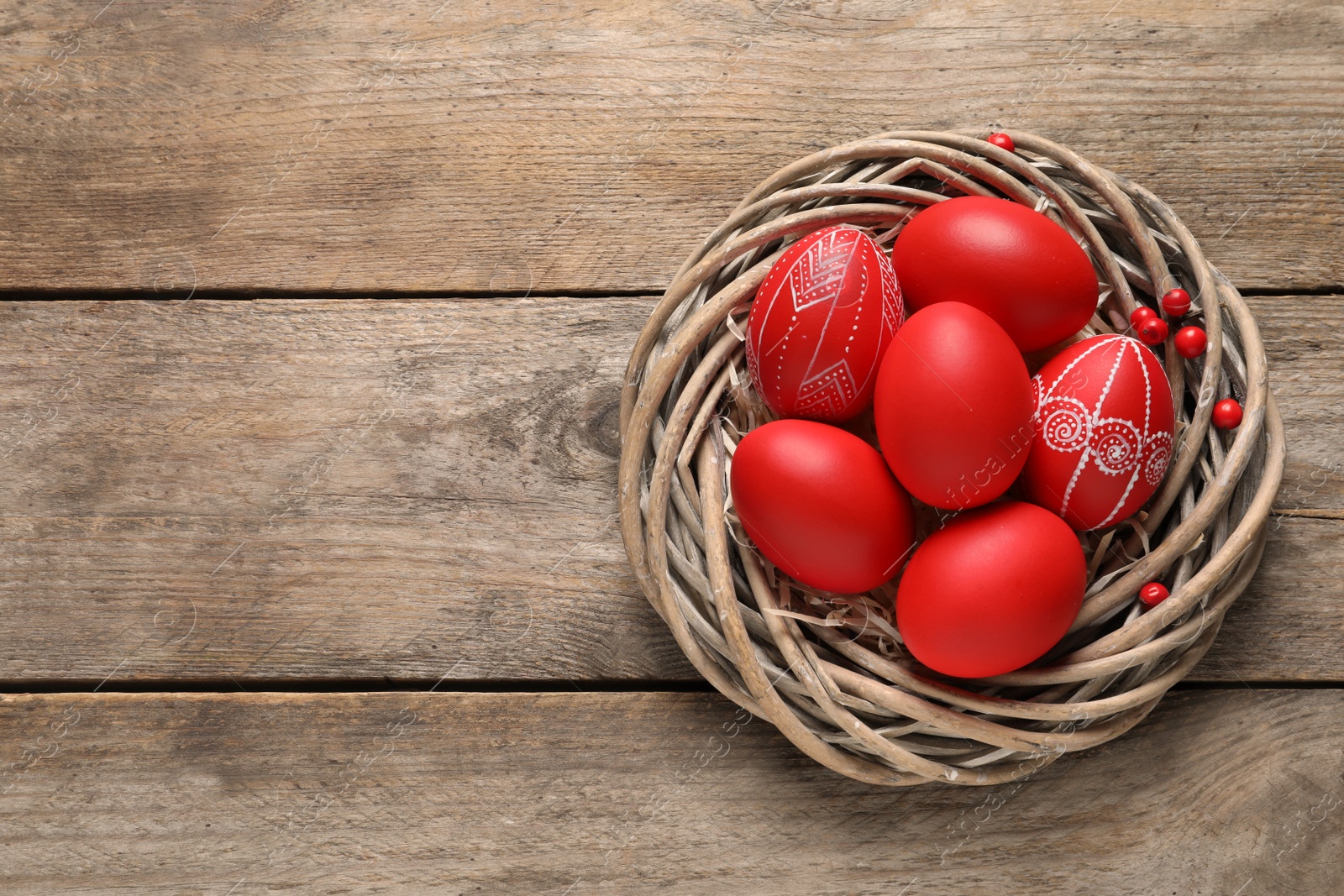 Photo of Wicker nest with painted Easter eggs on wooden table, top view. Space for text