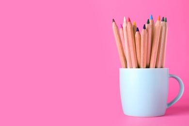 Colorful pencils in cup on pink background. Space for text