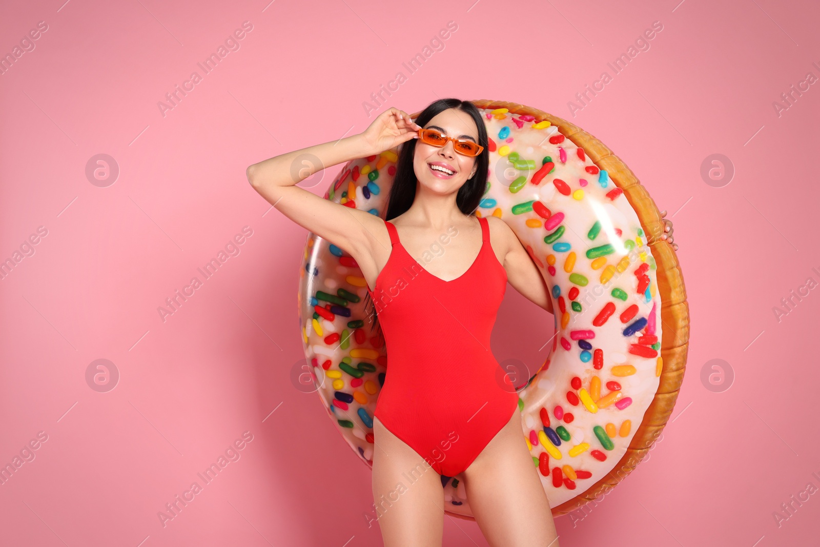 Photo of Young woman with stylish sunglasses holding inflatable ring against pink background