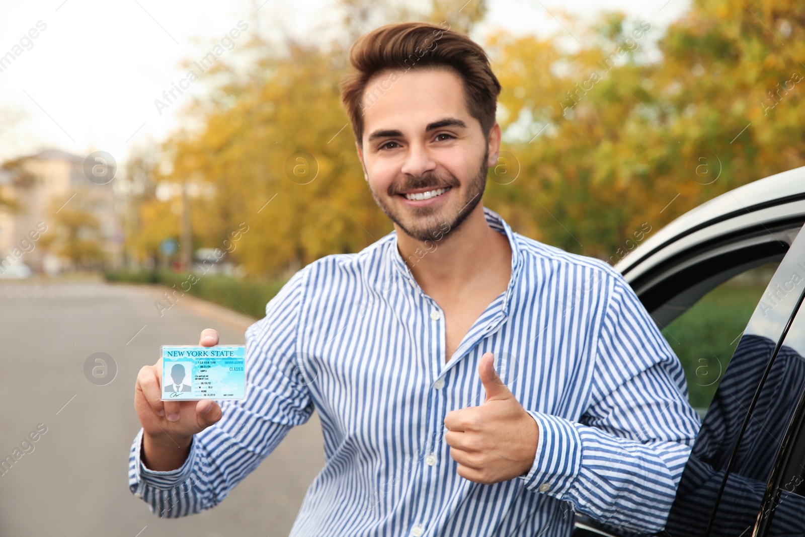 Photo of Young man holding driving license near open car