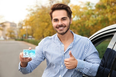 Young man holding driving license near open car