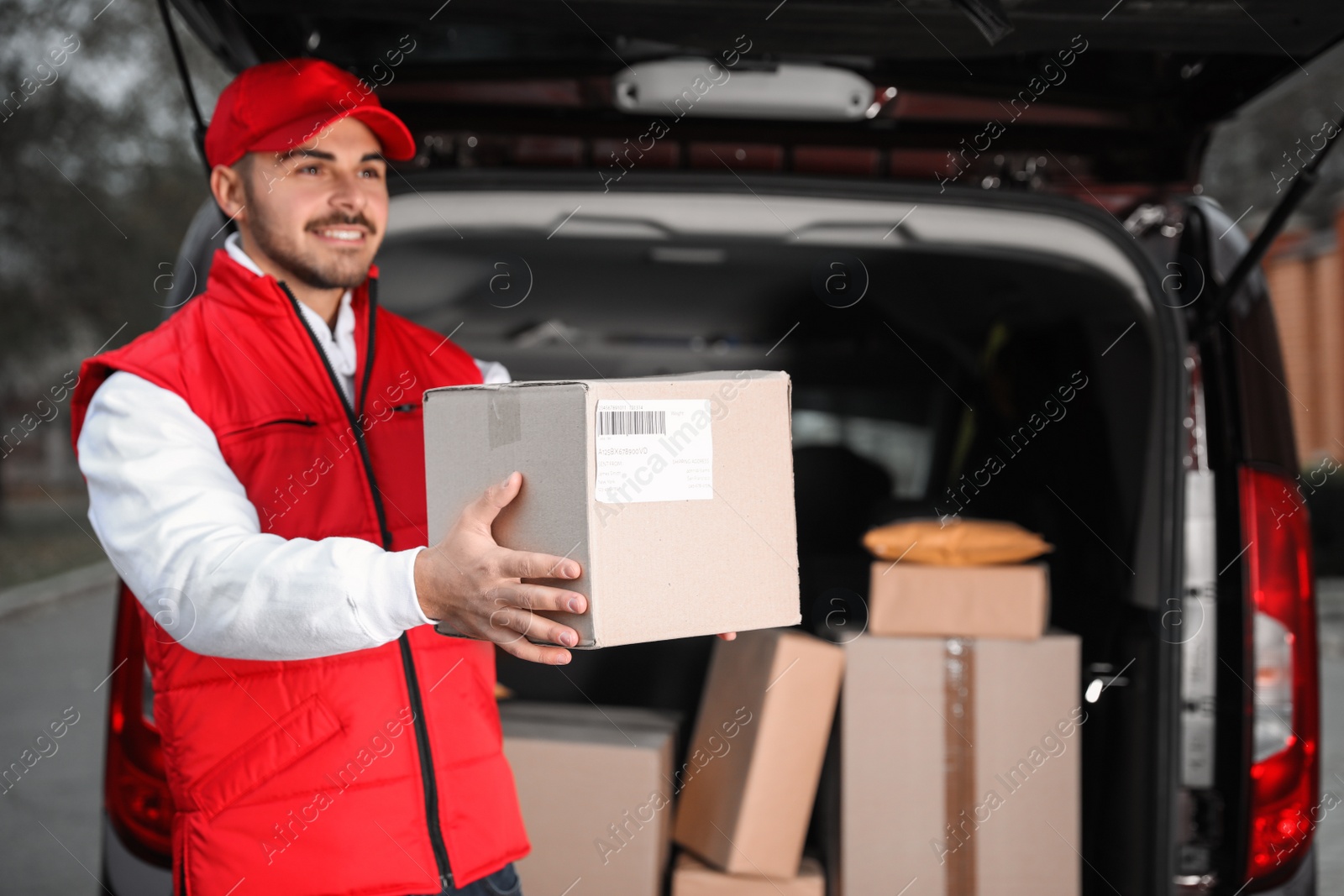 Photo of Deliveryman in uniform giving parcel near van outdoors