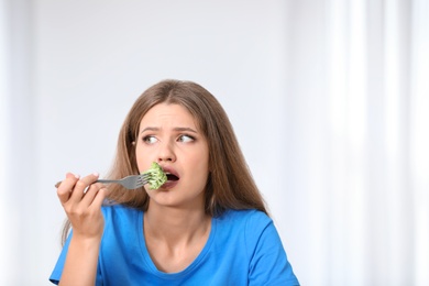 Photo of Portrait of unhappy woman eating broccoli on light background