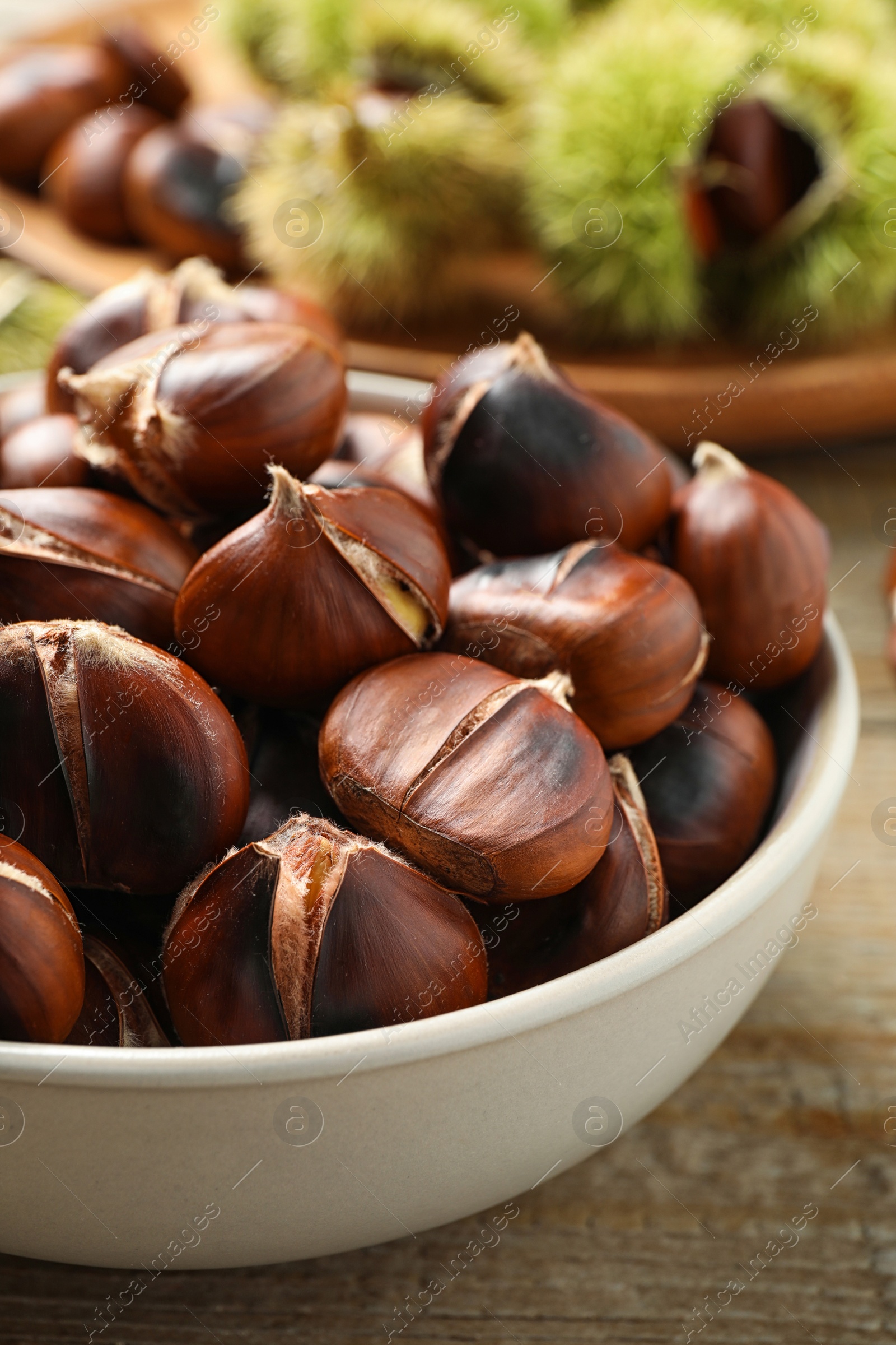 Photo of Delicious roasted edible chestnuts in bowl on wooden table, closeup